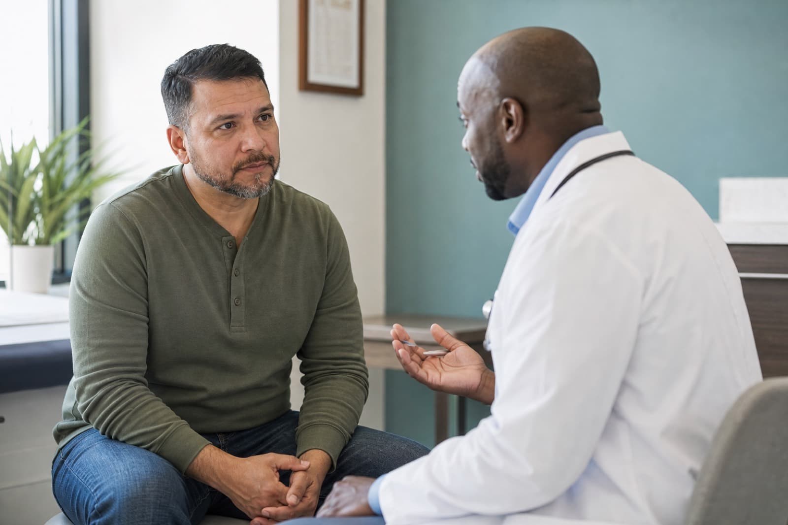 Adult man speaking thoughtfully with a clinician in a bright modern men's health consultation room
